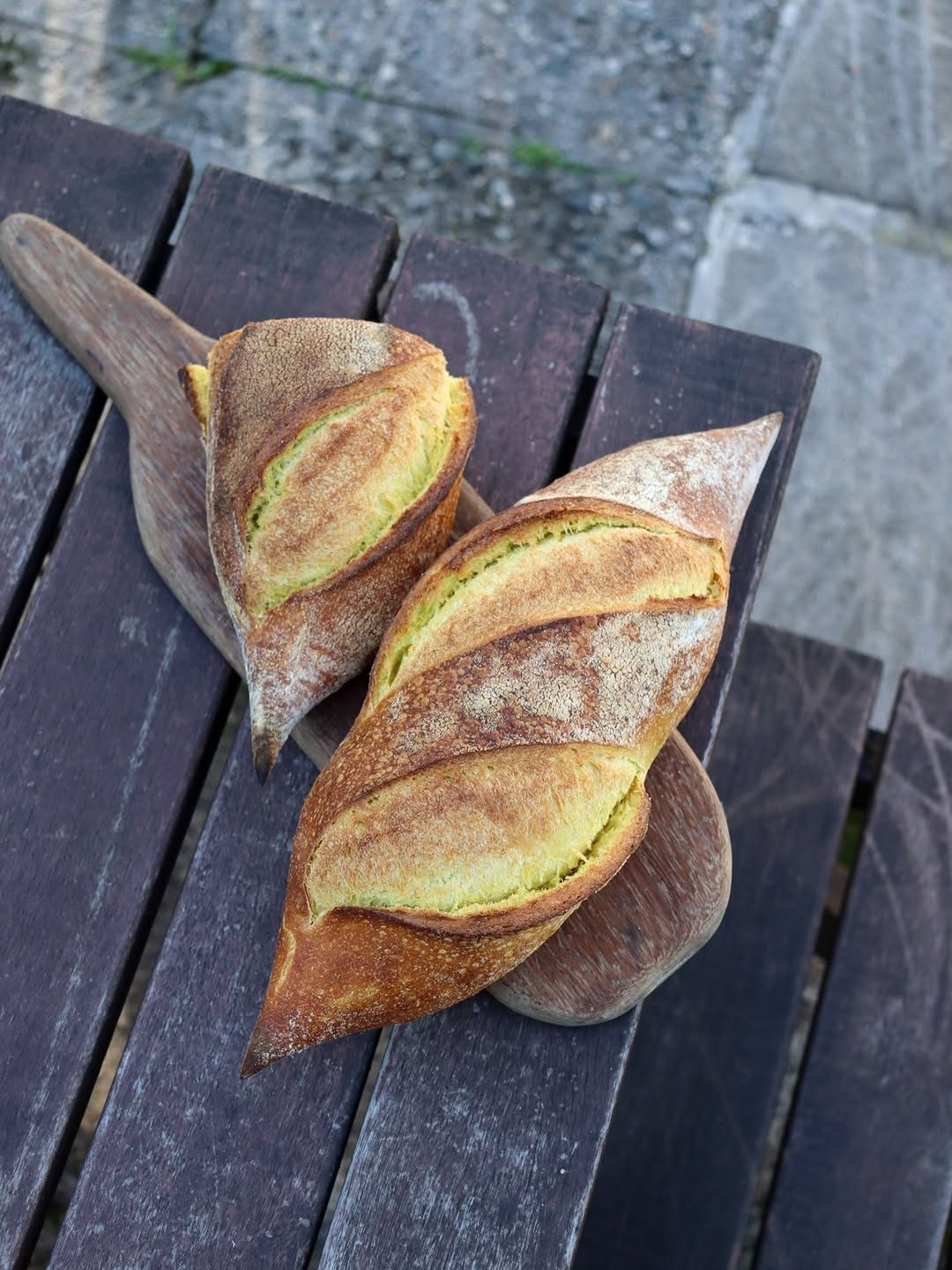 Dois pães de crosta dourada sobre uma tábua em mesa de madeira
