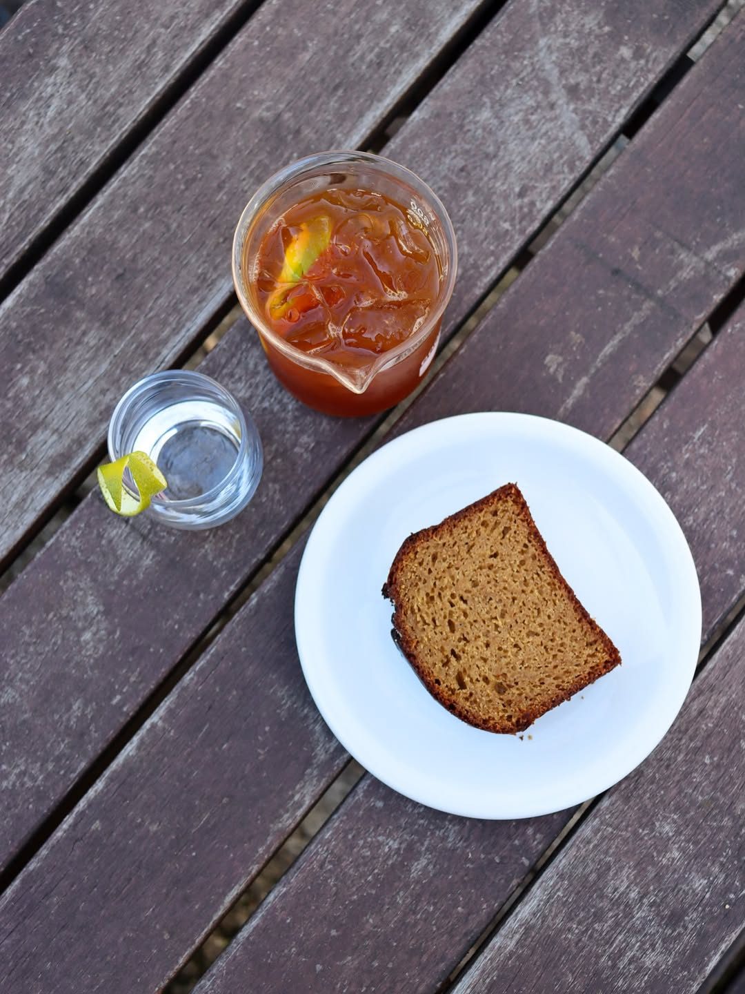 Bebida gelada, copo de água e fatia de bolo em prato branco sobre uma mesa de madeira